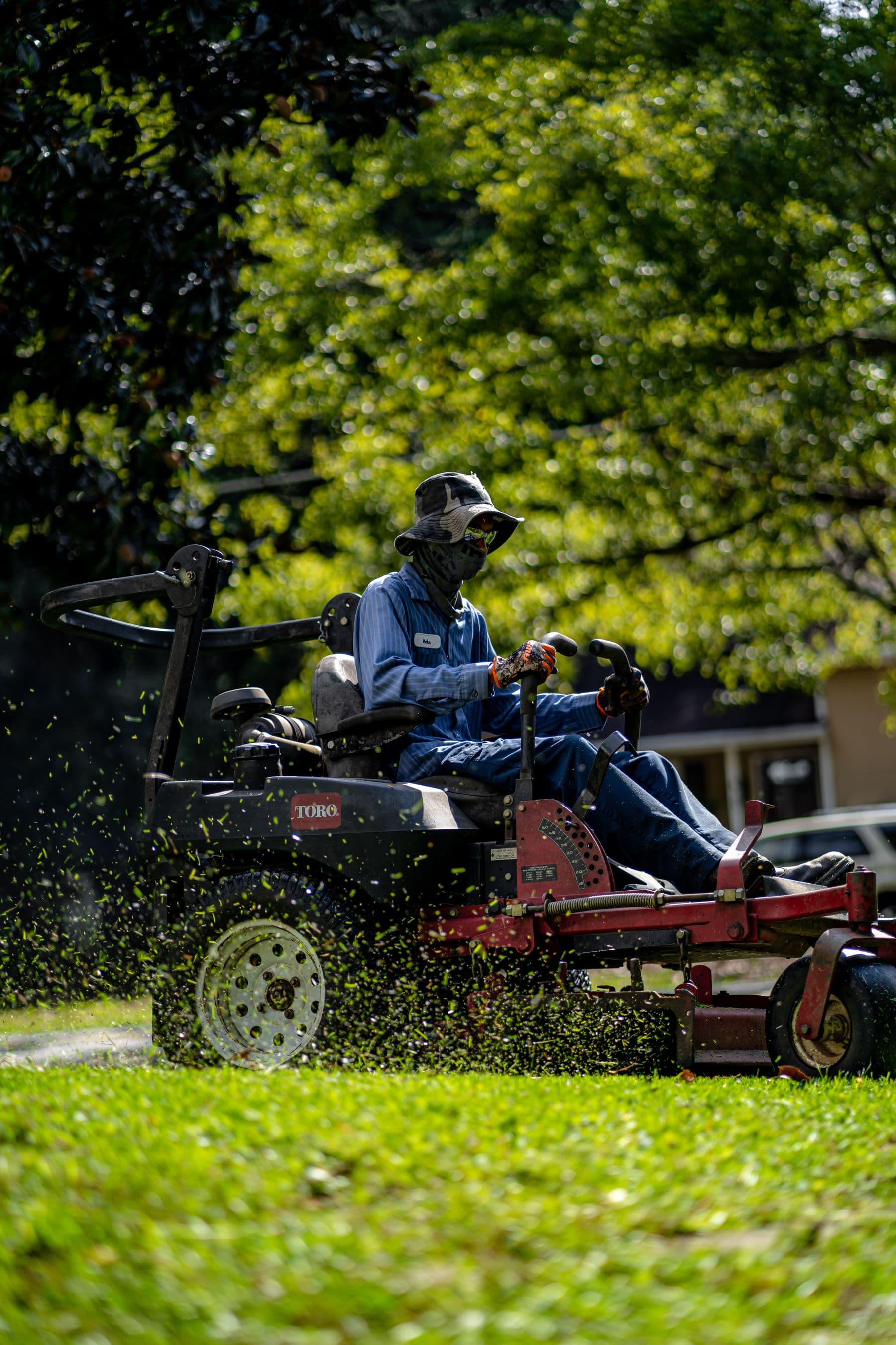 Crew member on a zero-turn mower cutting a striped pass, clippings in the air